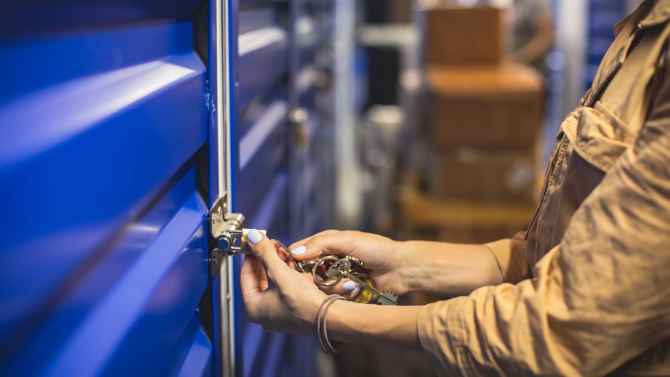 mid-level shot of a womans arm and hand unlocking a padlock on a self storage unit with blue doors